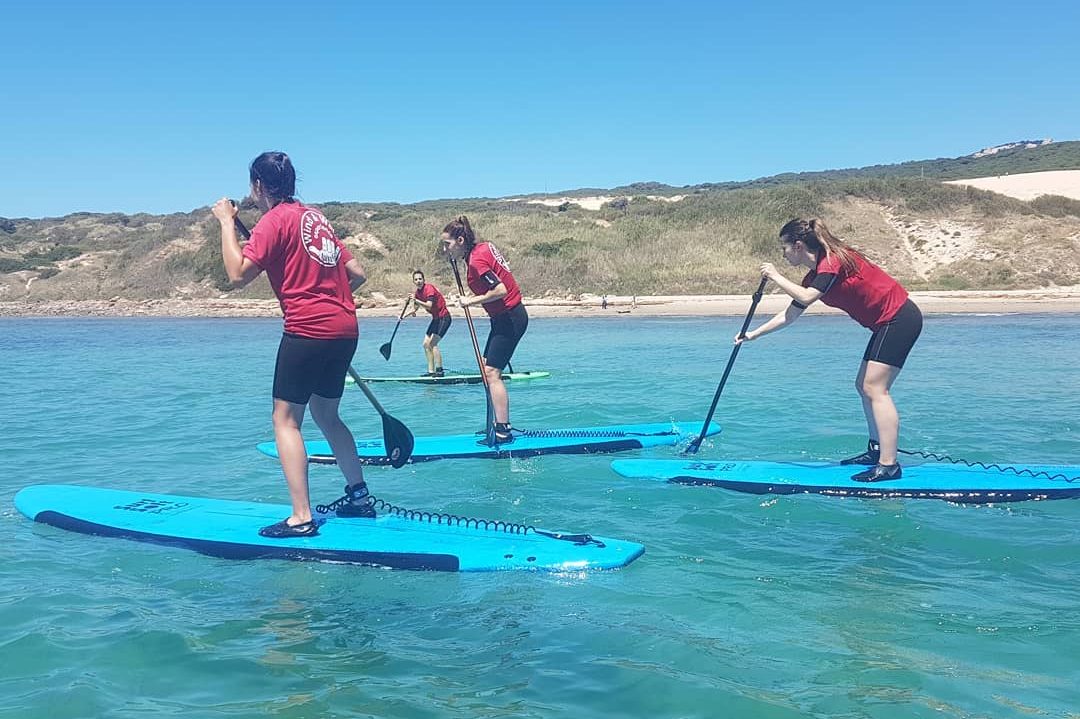 Alumnas de Wind & Water Experience de pie sobre la tabla durante una clase de paddle surf con remo en Tarifa.